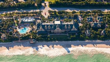 An aerial view of a resort with a large building, a swimming pool, and a beach.