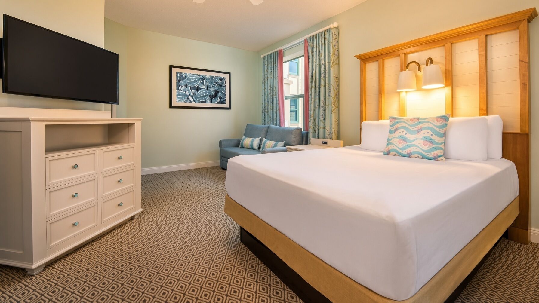 Une chambre d’hôtel avec un lit, une commode, un téléviseur, un tableau encadré et une fenêtre avec des rideaux.