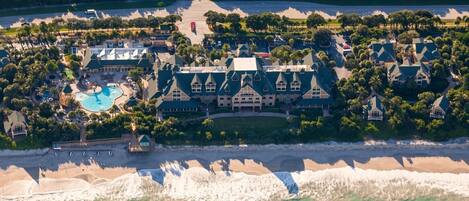 An aerial view of a resort with a large building, a swimming pool, and a beach.