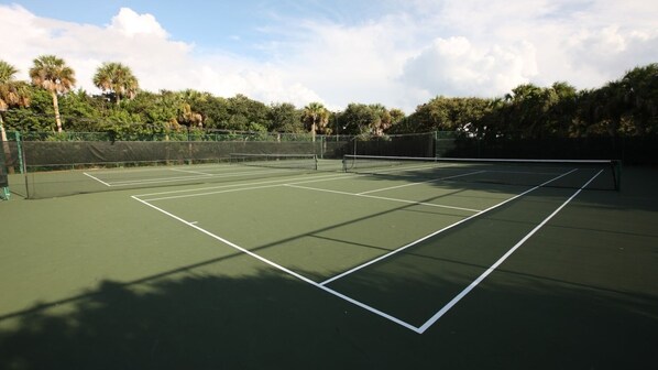 An outdoor tennis court with a net, surrounded by trees and a clear sky.