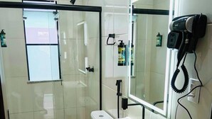 Une salle de bain moderne avec une douche à parois de verre, des toilettes, un lavabo avec un miroir et un sèche-cheveux fixé au mur.