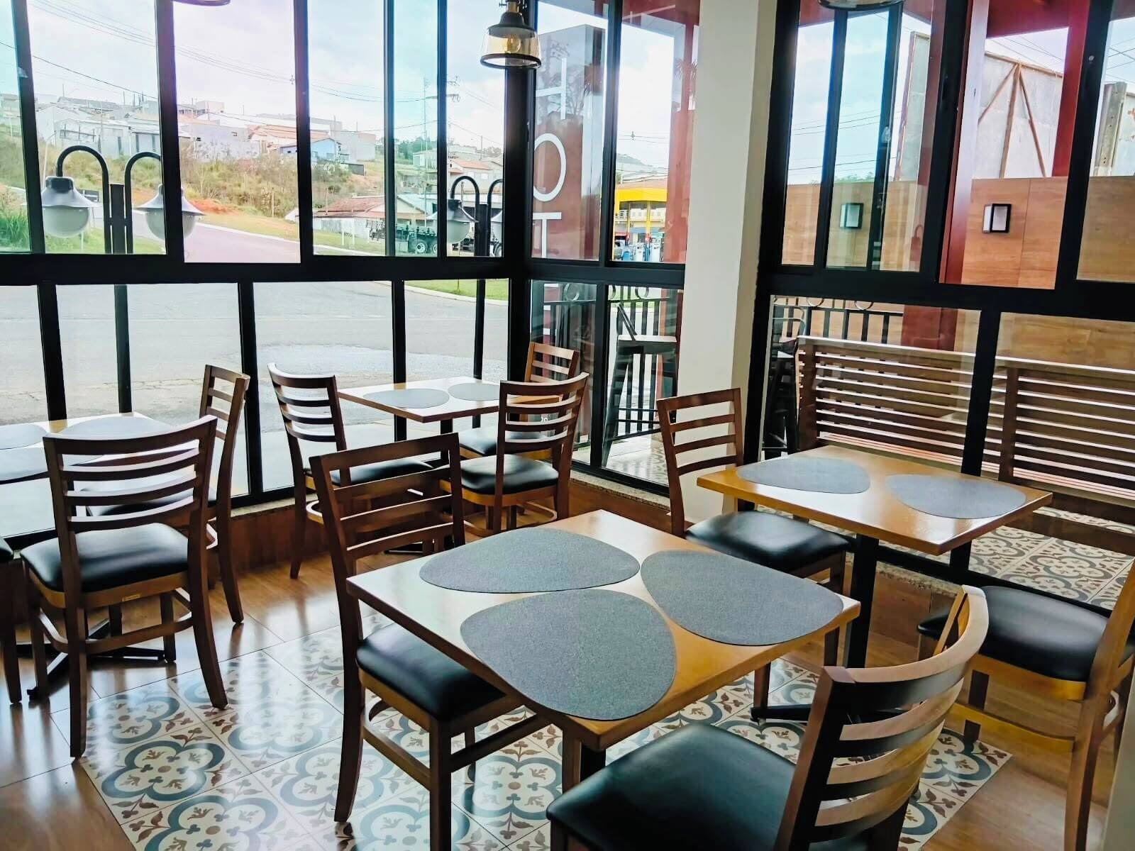 A restaurant interior with tables and chairs, large windows, and a view of the street outside.
