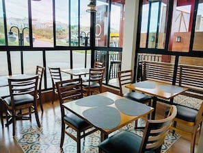 A restaurant interior with tables and chairs, large windows, and a view of the street outside.