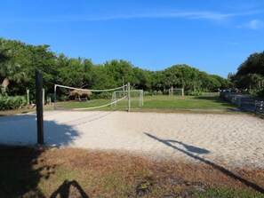 A volleyball court with a net, surrounded by sand and greenery.
