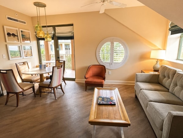 A living room with a dining table, chairs, a sofa, a coffee table, and a ceiling fan.