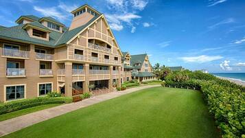 A multi-story hotel with a well-maintained lawn and a view of the ocean.