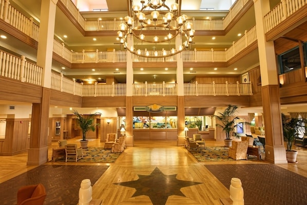 A multi-level hotel lobby with a grand chandelier, wooden railings, and a central reception desk.