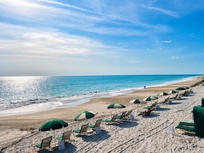 A beach with rows of sun loungers and umbrellas, a clear sky, and the ocean.