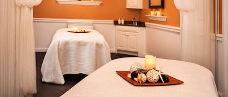 A hotel room with two beds, a small table with candles and decorative items, and a white cabinet.