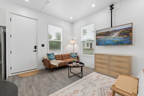 A modern living room with a sofa, a coffee table, a rug, and a painting on the wall. - Modern Boxabl Casita | Stillwater OK | Pasadera 7 (Stillwater)