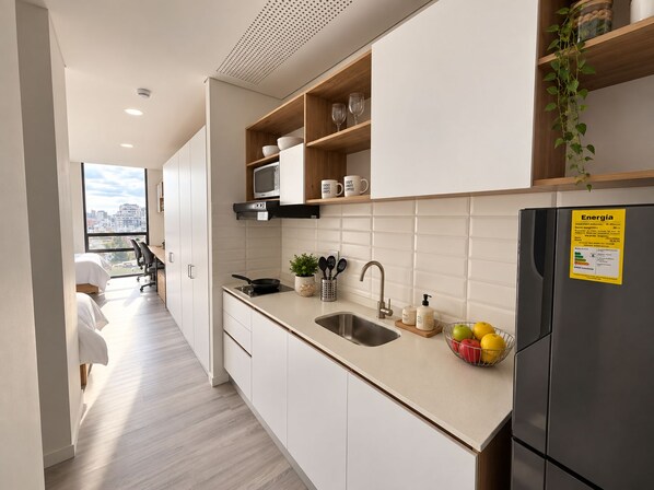 Una cocina moderna con armarios blancos, un lavamanos de acero inoxidable y un refrigerador negro.