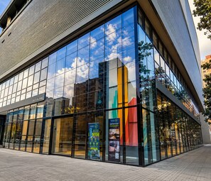 A modern building with large glass windows reflecting the sky and clouds. - Esstadia33DC (Bogotá)