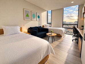 A hotel room with two beds, a sofa, a desk, and a view of the city. - Esstadia33DC (Bogotá)