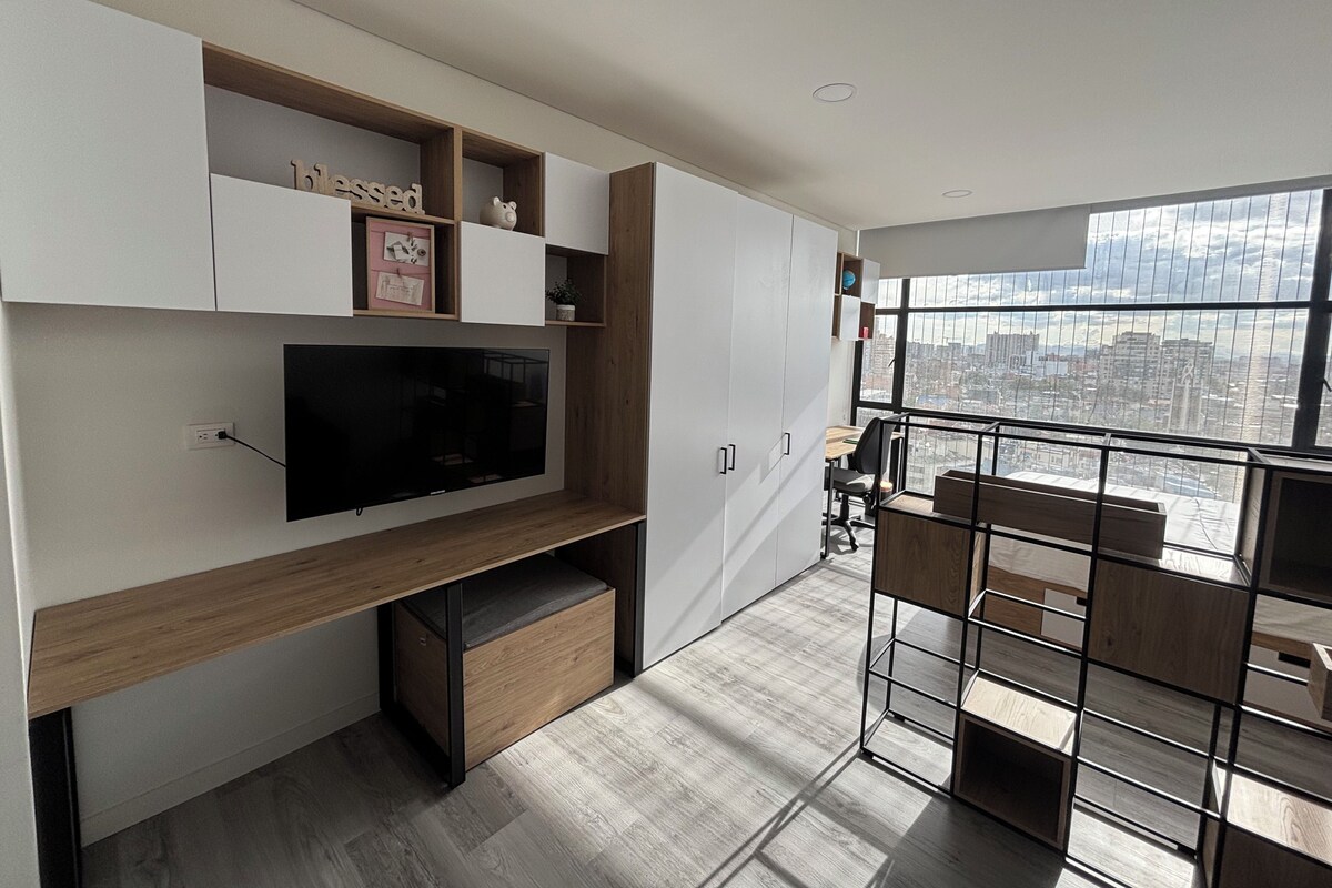 A modern interior with a flat-screen TV, built-in shelving, and a city view through large windows.