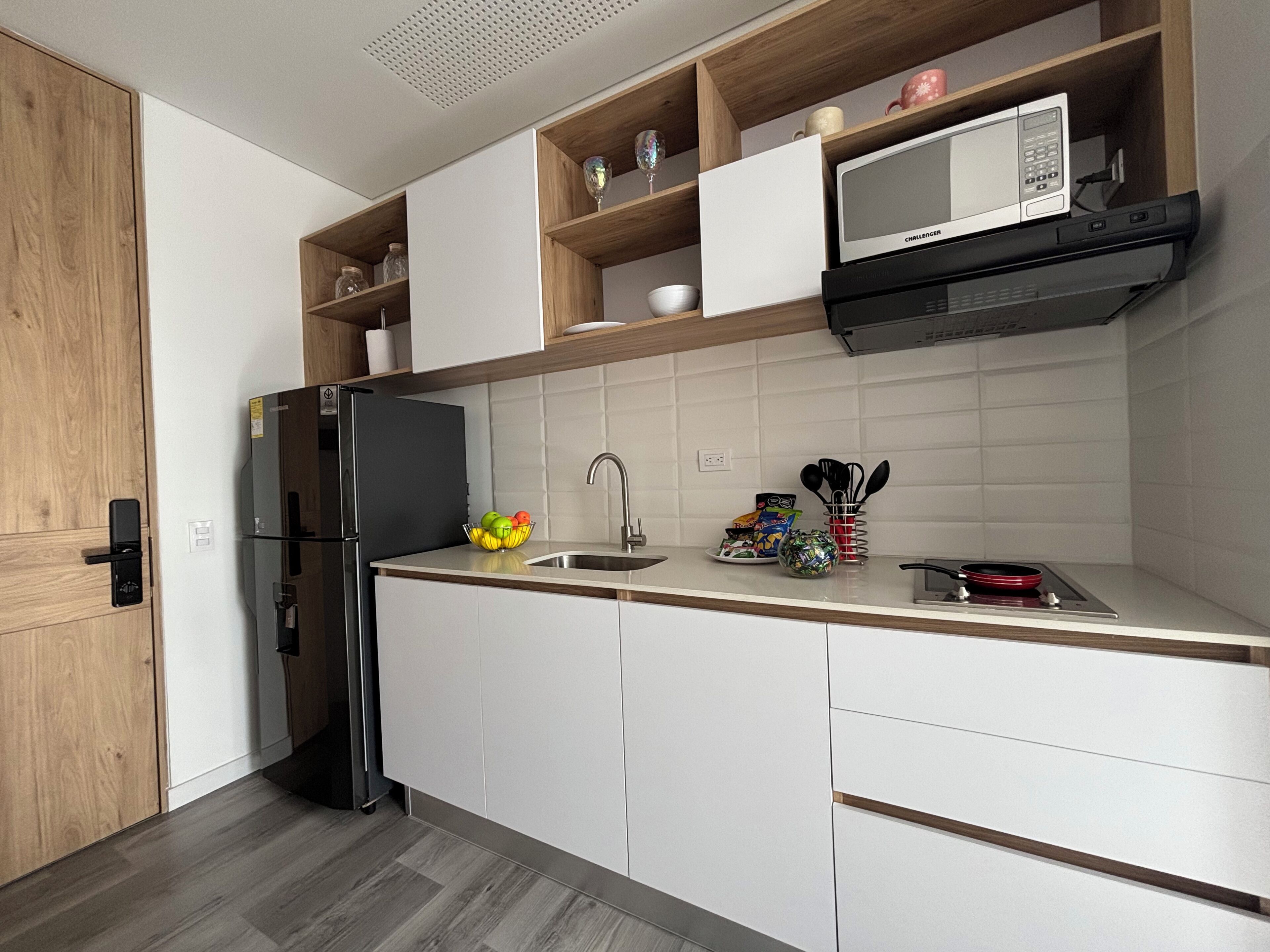 Une cuisine moderne équipée d’un four à micro-ondes encastré, d’un réfrigérateur en acier inoxydable et d’un meuble en bois.