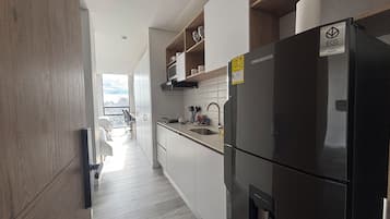 Et moderne køkken med et sort køleskab, hvide skabe og udsigt til opholdsstuen.