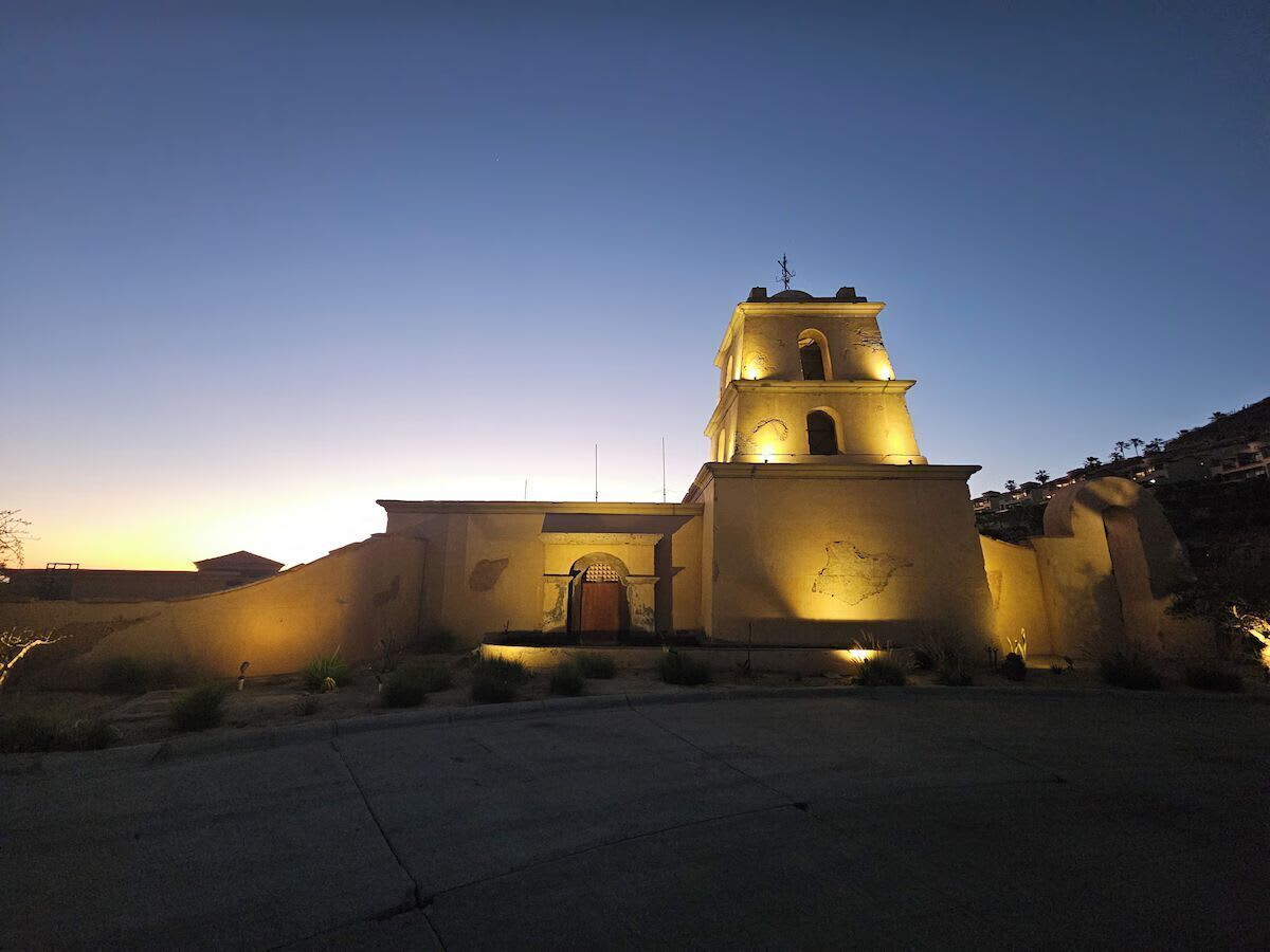 Um edifício com uma torre de sino, uma grande entrada em arco e um pátio.