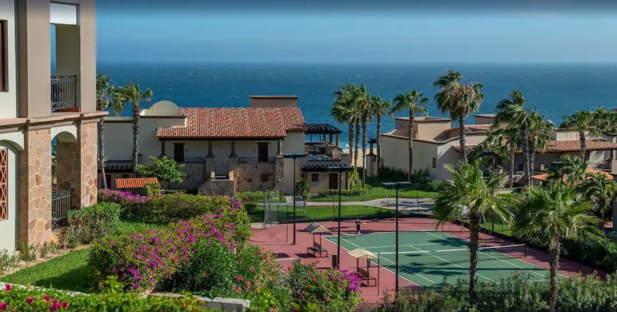 A residential area with a tennis court, palm trees, and a view of the ocean.