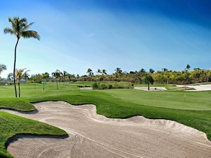 Ein Golfplatz mit Sandbunkern, grünen Fairways und Palmen.