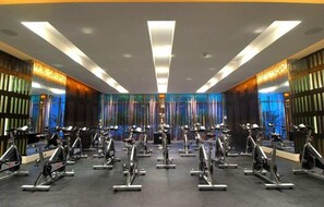 Ein Fitnessraum mit mehreren in Reihen angeordneten Ergometer, moderner Beleuchtung und einer großen Spiegelwand.