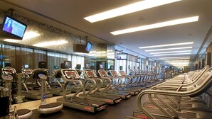 Una palestra con diverse tapis roulant disposti a file, un televisore montato a parete e uno specchio che riflette l'ambiente.