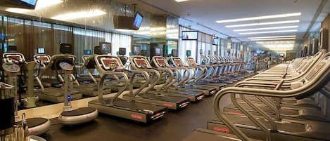 A gym with multiple treadmills arranged in rows, a television mounted on the wall, and a mirror reflecting the space.