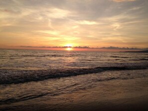 Ein Sonnenuntergang über dem Wasser, wobei Wellen auf das Ufer zulaufen.