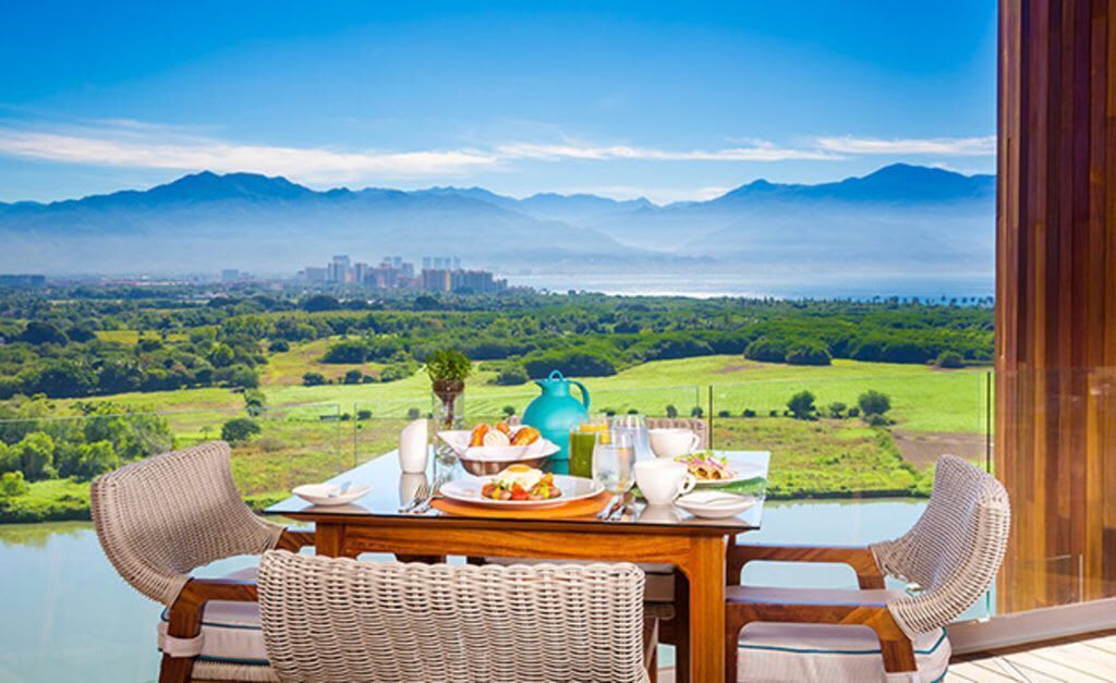A dining table with chairs and a view of a lake and mountains.