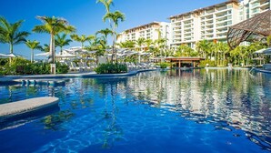 Ein Hotelpool mit klarem, blauem Wasser, umgeben von Palmen und einem mehrstöckigen Hotelgebäude.
