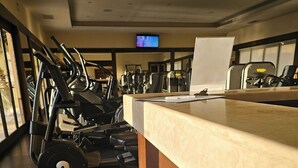 Uma academia com equipamentos de exercício, uma televisão na parede e um balcão com um quadro branco.