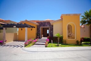 A two-story building with a stone facade, a covered patio, and a well-maintained garden with pink flowers. - Beautiful Oceanview Villa at Pueblo Bonito (Cabo San Lucas)