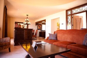 Un salon comprenant un canapé, une table basse et un meuble. Un lustre est suspendu au-dessus de la table.