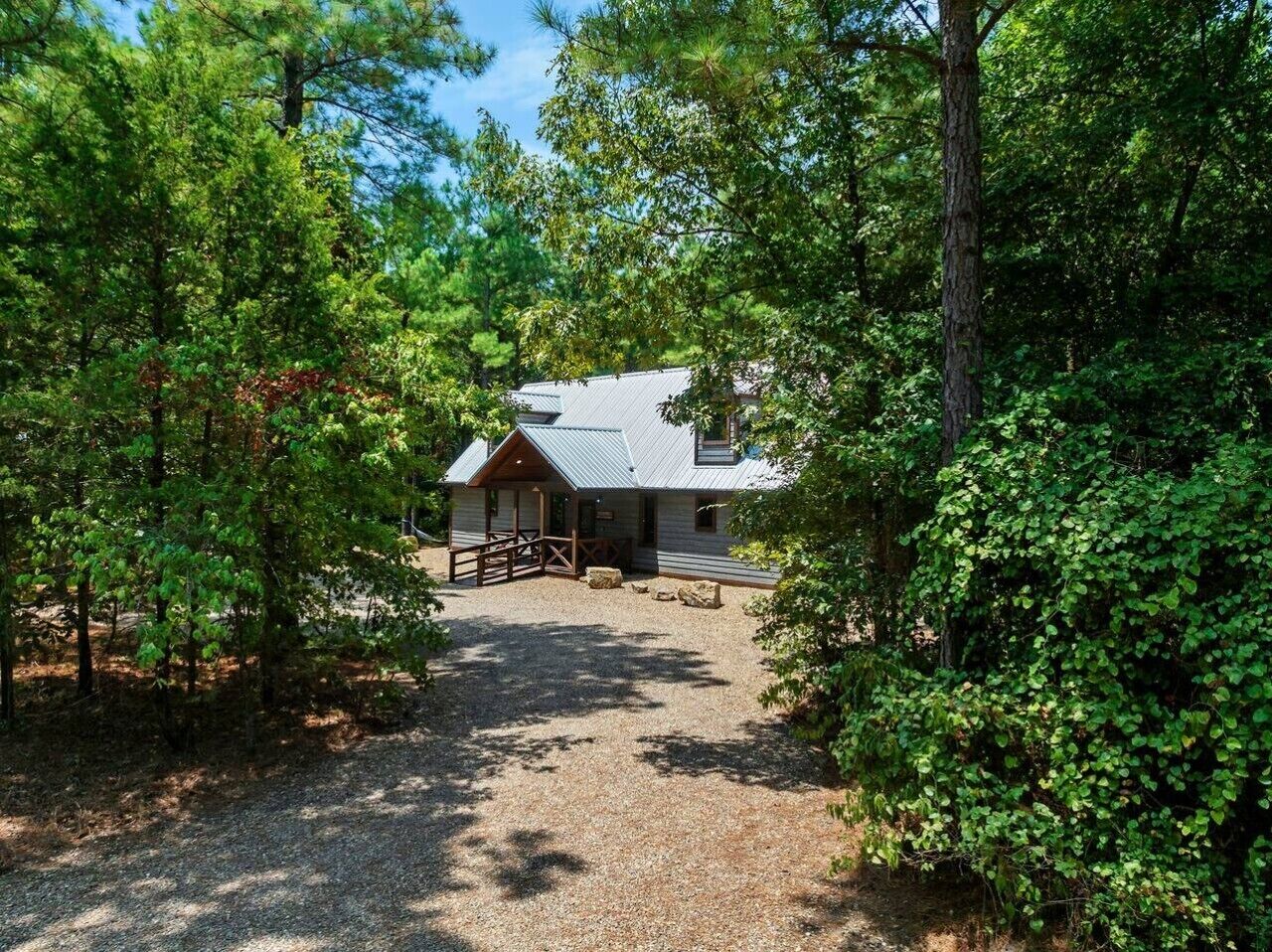 Un chalet rustique avec une allée en gravier, entouré d’une végétation luxuriante.