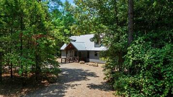 Un chalet rustique avec une allée en gravier, entouré d’une végétation luxuriante.
