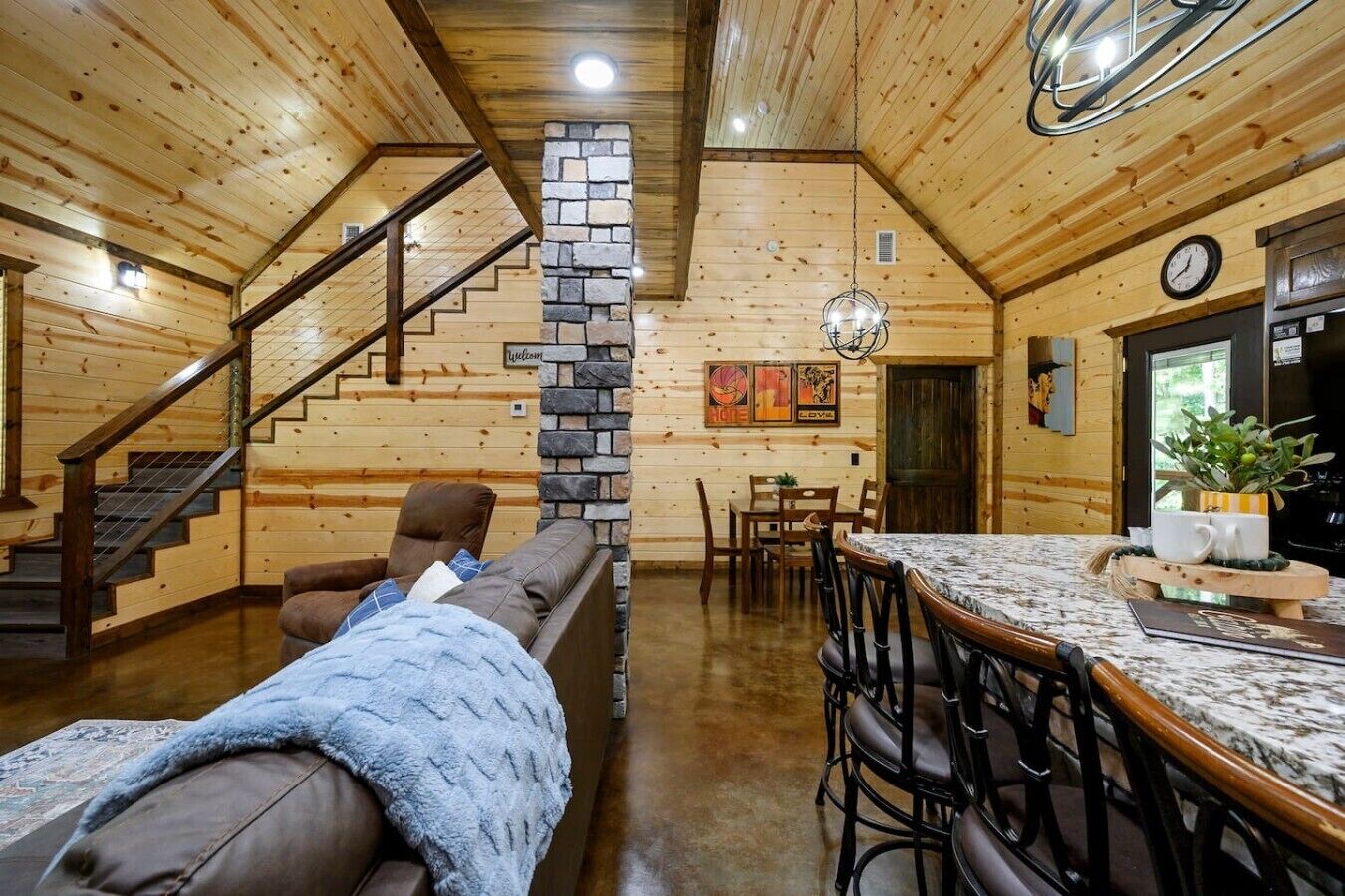 L’intérieur chaleureux d’un chalet avec une cheminée en pierre, des murs en bois, un coin repas et un escalier.