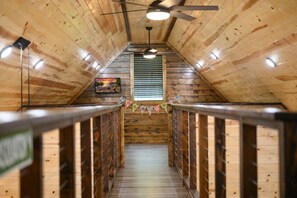 A wooden interior with a sloped ceiling, a central window with blinds, a ceiling fan, and a staircase leading to an upper level.