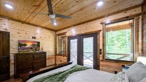 Een houten slaapkamer met een bed, een kapstok en een schilderij aan de muur.