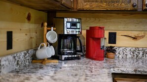 Een keuken met houten kastjes, een koffiezetapparaat en twee witte mokken op een marmeren aanrecht.