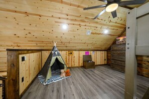 A room with a sloped ceiling, wooden walls, a tent-like structure with a bed inside, a dresser, and a ceiling fan. - The whole family will love The Rusty Rose Retreat (Broken Bow)
