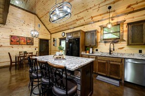 A kitchen with a central island, wooden cabinets, stainless steel appliances, and a hanging light fixture. - The whole family will love The Rusty Rose Retreat (Broken Bow)
