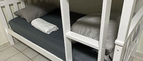 En våningssäng med madrass och kuddar, en hopvikt handduk och en vit ram.