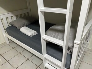 A bunk bed with a mattress and pillows, a folded towel, and a white frame. - Davish house (Hialeah)