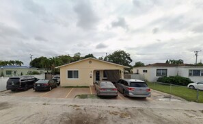 A small single-story building with a beige facade, a garage, and a parking lot with several cars. - Davish house (Hialeah)