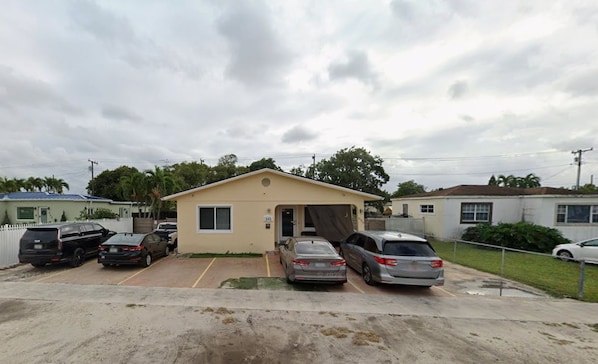 A small single-story building with a beige facade, a garage, and a parking lot with several cars. - Davish house (Hialeah)