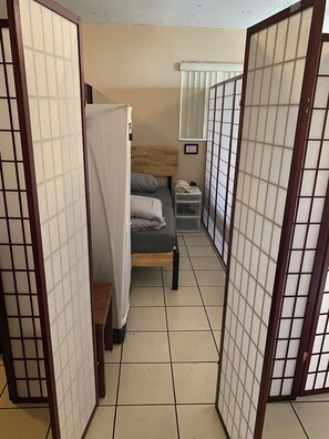 A room with a bed, a small bedside table, a wall-mounted shelf, and a sliding door with a grid pattern. - Davish house (Hialeah)