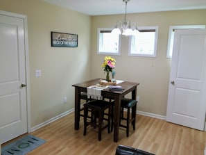 A dining area with a wooden table, two chairs, a chandelier, and a welcome sign on the wall.