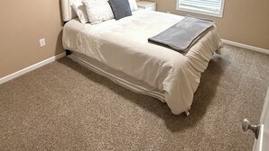 Une chambre à coucher avec un lit, une table de chevet, une fenêtre avec des stores et un luminaire au plafond.