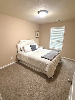 A bedroom with a bed, a nightstand, a window with blinds, and a ceiling light.