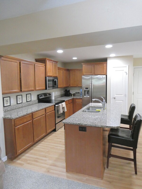 A kitchen with wooden cabinets, granite countertops, stainless steel appliances, and a central island with seating.
