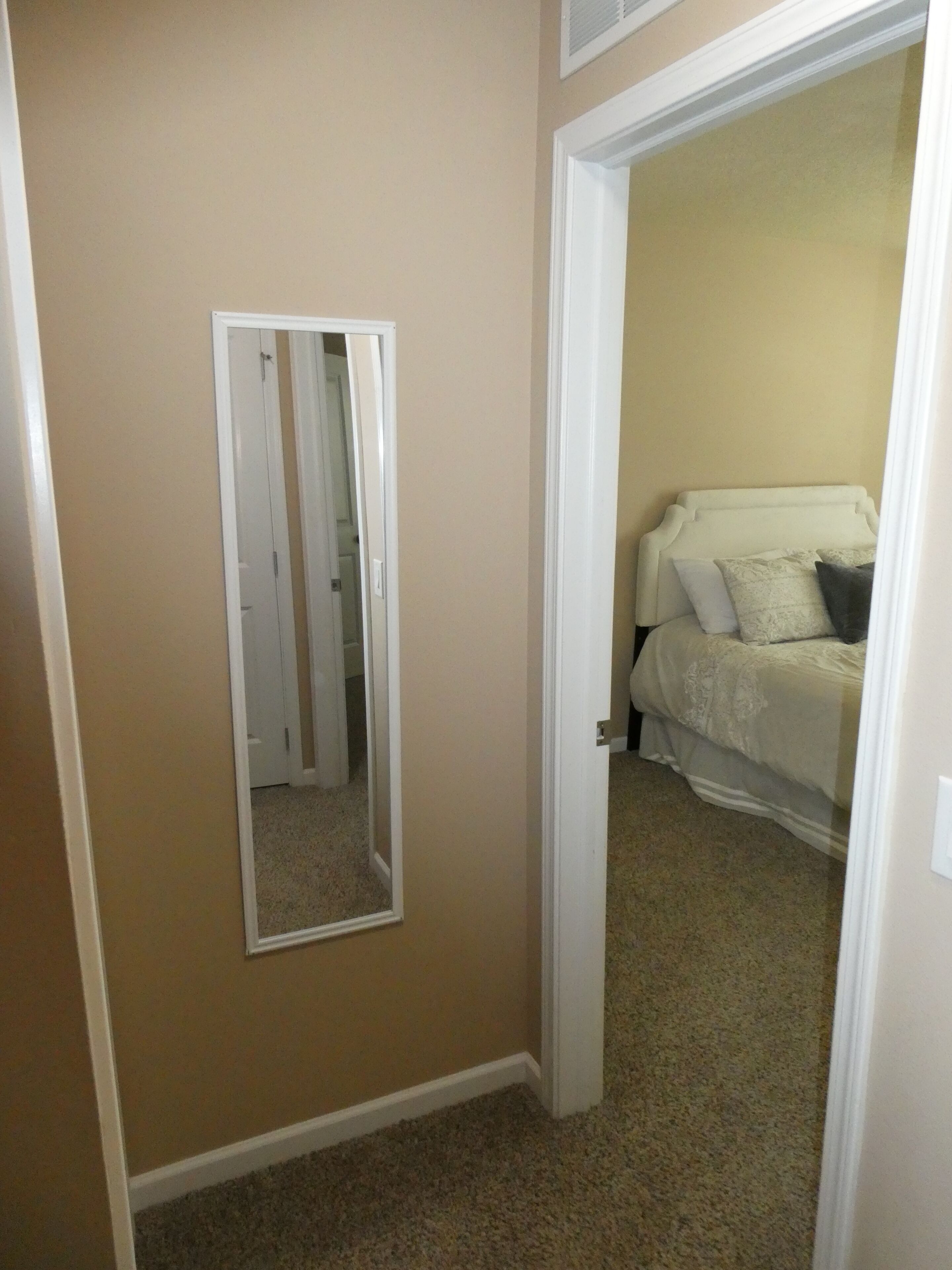 A room with beige walls, a white door, and a bed with a white headboard.
